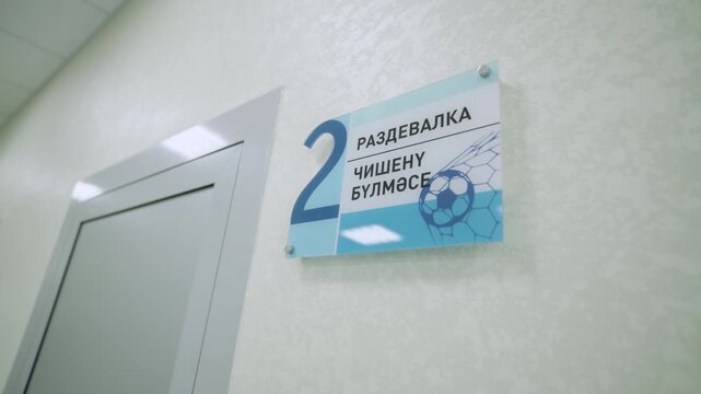 Glass directional sign hangs near door leading to changing room. Navigation within contemporary sports complex for visitors convenience