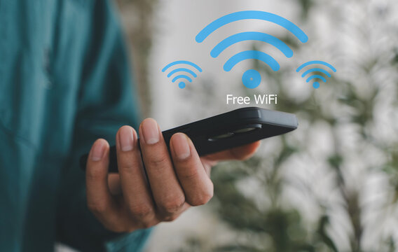 Close up of businessman hand holding smartphone with glowing free wifi network icon. Wireless internet access and digital communication technology concept. Mobile connection