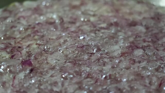 Detailed macro view of chopped red shallots frying continuously in hot bubbling vegetable oil, filmed in smooth slow motion for cooking and recipe content.
