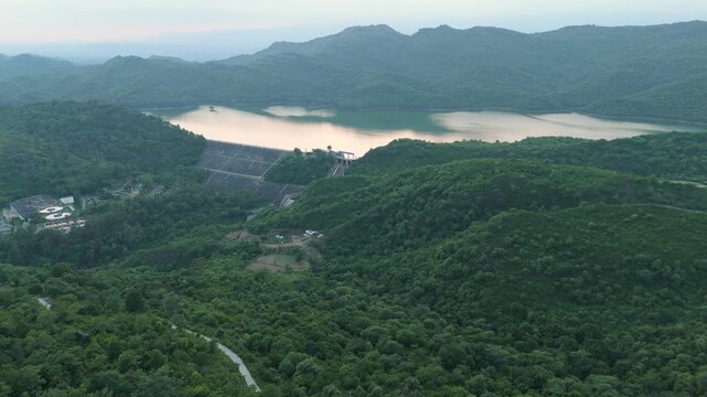 Aerial footage over forested mountains and camera slowly tilting down to reveal the Simli Dam and water reservoir in Margallah Hills of Islamabad, sunset reflection in water