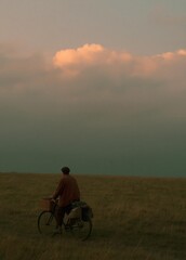 Fototapeta premium Man riding a bicycle on a grassy field. he is wearing a brown jacket and a cap, and has a basket attached to the back of the bicycle.