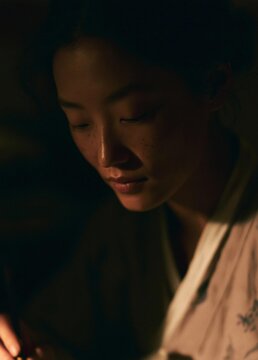 Close-up portrait of a young woman's face. she appears to be deep in thought, with her eyes closed and her head tilted downwards. the lighting is dim, creating a moody and contemplative atmosphere.