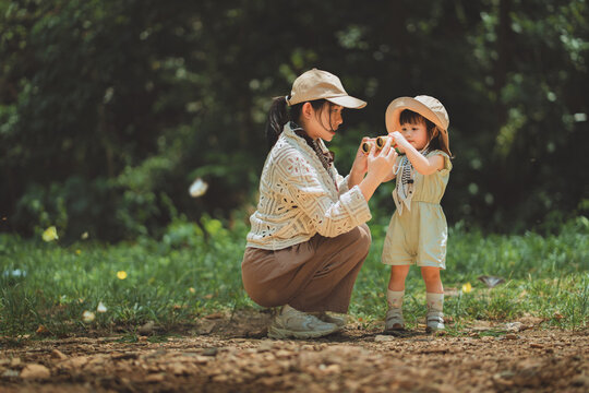Mother teaching young daughter how to use binoculars outdoors, learning and exploring nature together