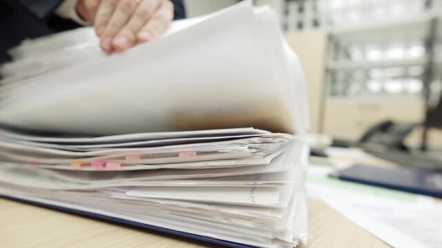 Thick stack of white document pages lies on office desk. Blue folder cover protects heavy archive files from dust damage. Office paperwork
