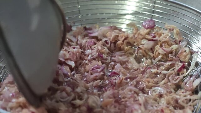 Macro slow motion video of sliced shallots sizzling inside a wire basket skimmer held in hot oil, then lifted up to drain excess oil before serving.
