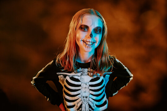 Portrait of Caucasian teenager girl wearing skeleton costume and spooky face paint smiling during Halloween celebration. Image suitable for seasonal marketing campaigns