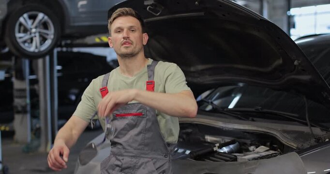 Portrait of a skilled car mechanic in a workshop, with service in the background.