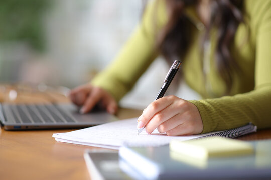 Student hand taking notes and using laptop on a table