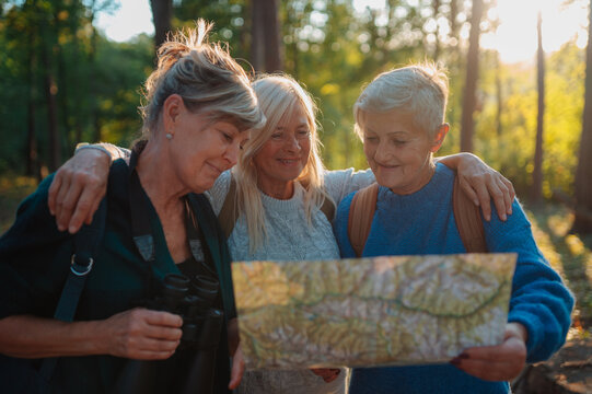 Mature female friends exploring nature together with map on hiking trip.