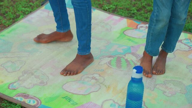 Barefoot mother and child on mat closeup feet on colorful play mat outdoors, wearing jeans, water bottle placed as focal marker, gentle stepping and balance practice, playful teaching moment, warm