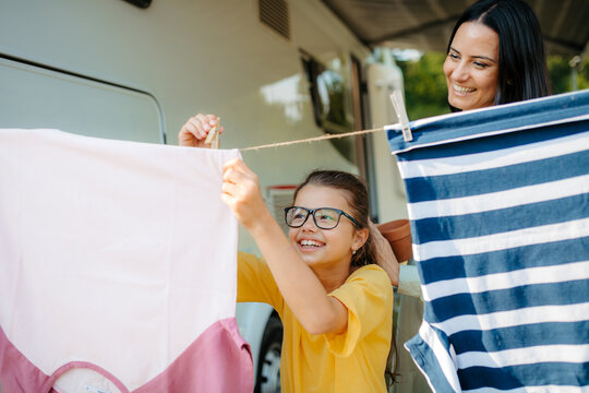 Mother and daughter hanging laundry beside camper on family vacation.