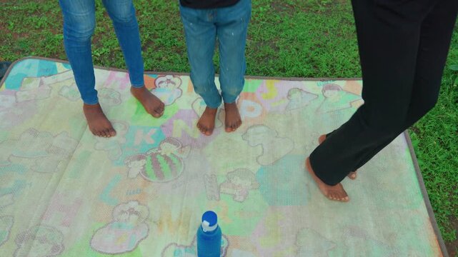 Children enjoying active family games. Playful family outdoor activity with energetic kids. Vibrant family exercise session on patterned blanket with water bottles and cheerful atmosphere