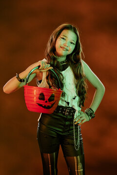 Portrait of Asian teenager girl wearing Halloween costume holding pumpkin bucket. Image ideal for seasonal marketing campaigns and holiday event promotions, vertical