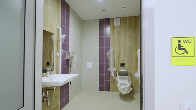 Modern accessible bathroom features purple and wood tiles near sink with wrapped handrails. Bright public facility layout looks organized