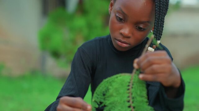 Black child hands exploring green plant closeup focus on leaf and stem studious expression backyard grass and blurred shrub backdrop young gardener role implied curiosity and learning captured