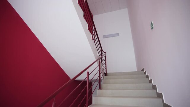 Clean indoor staircase features wide steps and metal railings. Angular architecture combines sharp lines with deep maroon accent wall