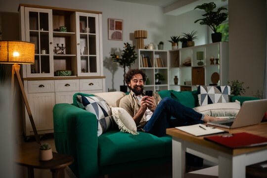 Man relaxing on sofa using smartphone at home
