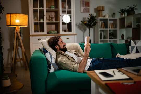 Man relaxing on couch reading book at night