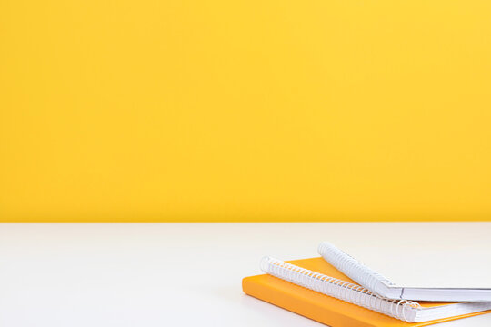 Orange and White Notebooks on a White Desk Surface Against a Yellow Wall. Minimalist Office Background for Education, Study, and Planning with Large Copy Space for Text. Business Banner.