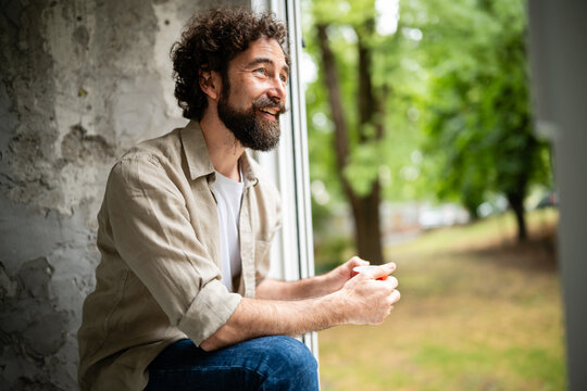 Happy man relaxing, enjoying coffee by window