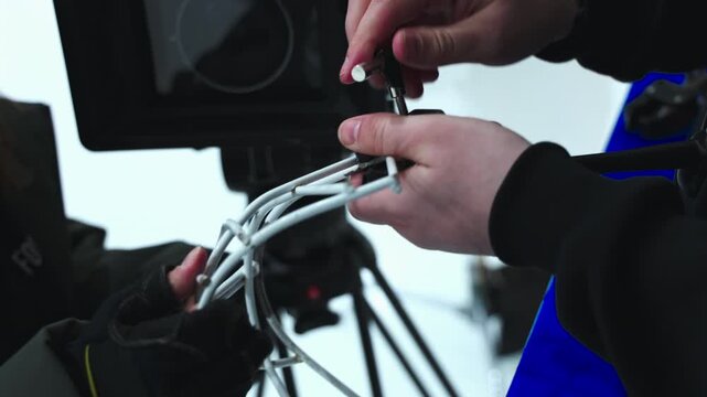 Hands use metal clamp tool to fix steel gear. Technical assistant attaches white decorative curved wire structures to studio stand