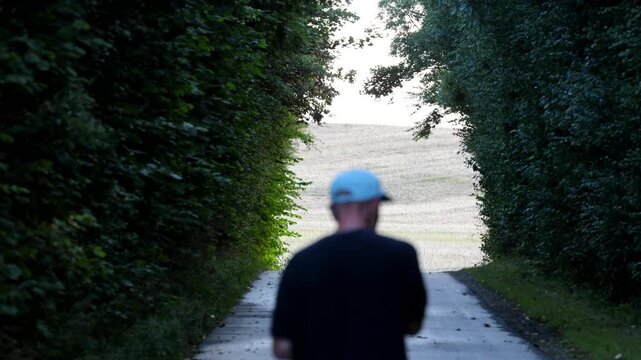 Tornby Bjerg, Denmark A man walks through a pastoral green and hilly landscape at sunrise through a thicket of trees. 