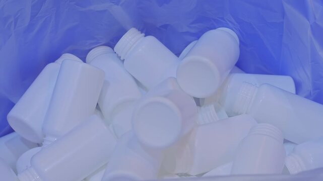 Empty white plastic bottles are falling into a large pile, heap from conveyor belt of bottle injection blow molding machine at factory, plant - close up