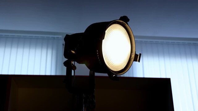 Powerful video light spotlight shines brightly in dark studio room. Fresnel lens element creates focused beam output direction path