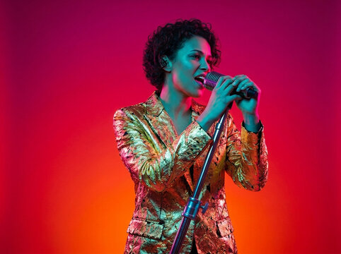 Singer in sequin jacket performs with microphone under colorful lights