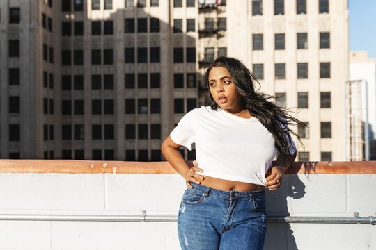 Person in casual attire poses on a rooftop with city buildings in the background.
