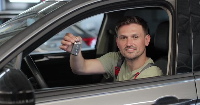 In a car repair garage a mechanic after settling the car shows the keys as a car ready to start. Automotive industry, auto care, service.
