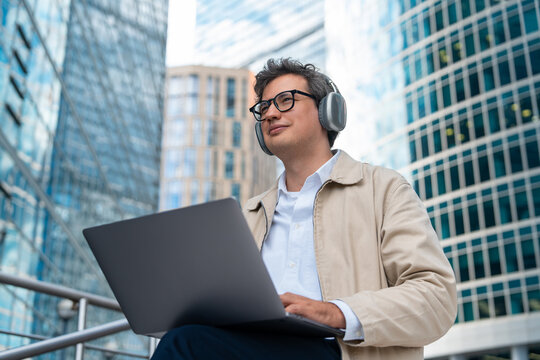 Businessman using laptop and wearing headphones among modern off