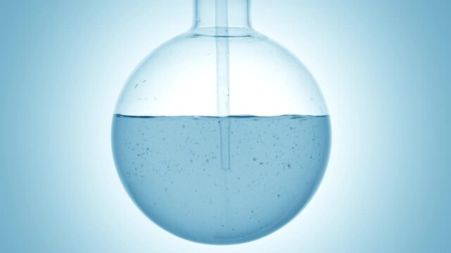 Close shot of light transparent blue liquid injected through a long dropper into a round-bottom flask, causing swirls and bubbles set on a smooth blue curved ramp