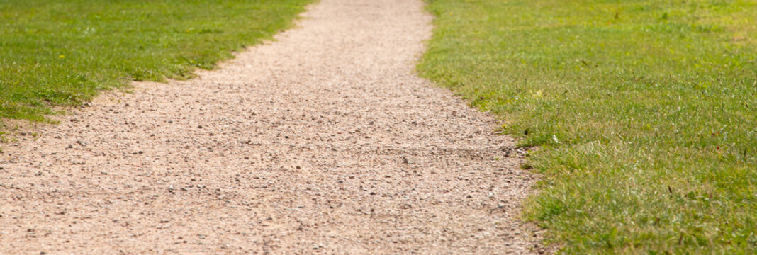 Gravel footpath walkway leading through green grass field in park background