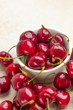 Bowl of red cherries sits on a table surrounded by more cherries picked from a tree