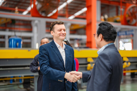 Factory executives shake hands on production floor while employees applaud, showing business partnership, agreement, leadership, manufacturing management, teamwork.