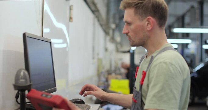 Car mechanic using computer to run diagnostic software for troubleshooting engine problems, modern computerised automotive repair.