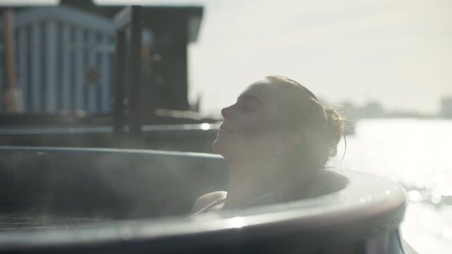The woman enjoys a peaceful morning soak in an outdoor spa by the waterfront