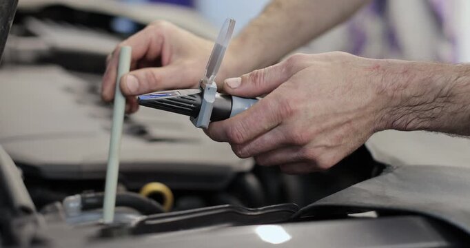 Close up hand of auto mechanic checks the quality of antifreeze in a car and other diagnostic procedures. Automotive industry, auto care, service.