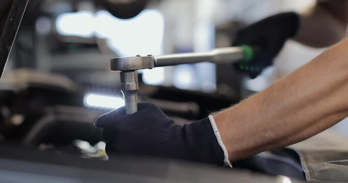Hand of mechanic man using socket spanner wrench repairing a car in workshop at auto car repair service center. Car engineer inspection vehicle details.