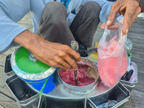 Indonesian street vendor's hands packing traditional pink cotton candy into a plastic bag. Ideal for editorial articles, culinary blogs, cultural documentary presentations, and travel website design