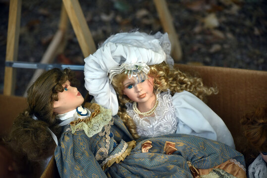 Two elegant retro dolls wearing beautiful vintage dresses displayed among old objects at a flea market, creating a nostalgic atmosphere around childhood and collectible toys.

