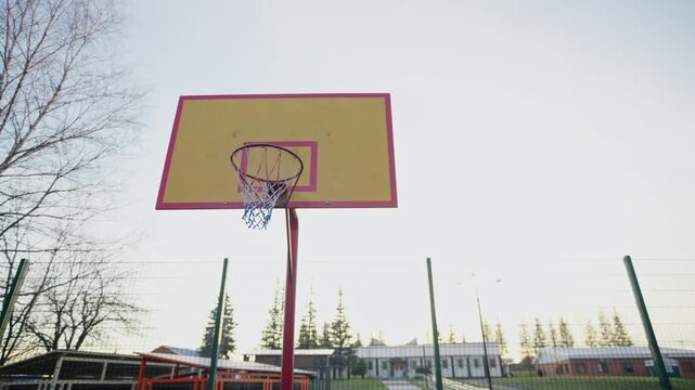 Tall metal basketball pole holds rectangular wooden backboard high. Morning sky highlights simple athletic equipment in recreation park