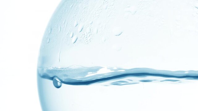 Pale blue transparent fluid boiling in a round-bottom flask, producing bubbles, waves and condensation on its wall against plain white | Mineral water beauty ingredient concept