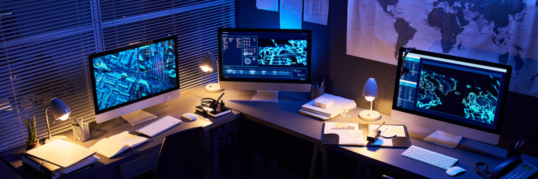 Empty cybersecurity control room desks with multiple computer monitors displaying digital maps and data. Concept of global surveillance and network security, wide shot