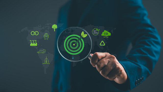 A person in a suit holds a magnifying glass focusing on a green target with an arrow, surrounded by eco-friendly icons on a digital world map.