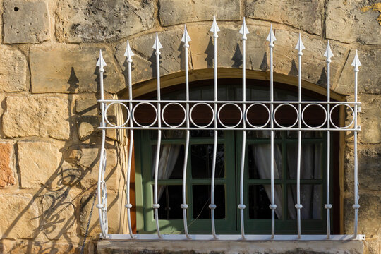 Green Arched Window With Decorative White Wrought Iron Bars On Rustic Stone Wall In Sunlight