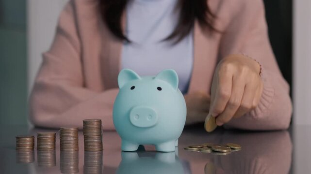 Financial saving concept. Closeup of a woman putting a coin into a blue piggy bank with stacked coins. Ideal for banking, investment, retirement planning. saving money and financial business.