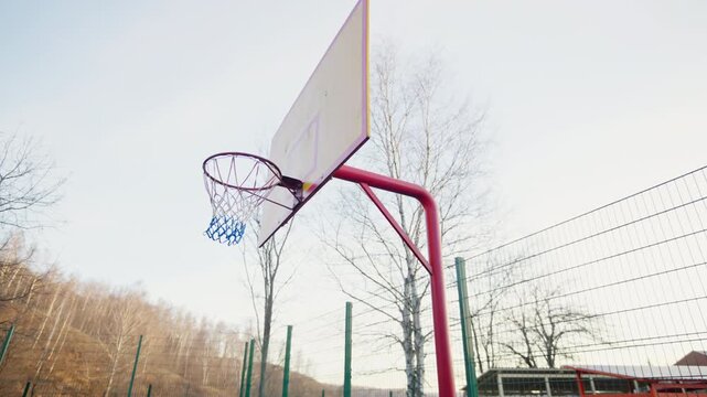 Net hangs from basketball rim on quiet basketball court. Golden outdoor scenery creates calm athletic environment. Outdoor sports equipment