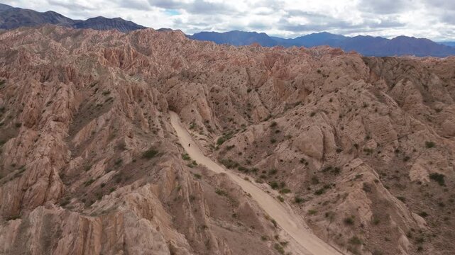 Motorbike traveling winding road through Quebrada de las Flechas rock landscape, aerial, Salta Region Argentina